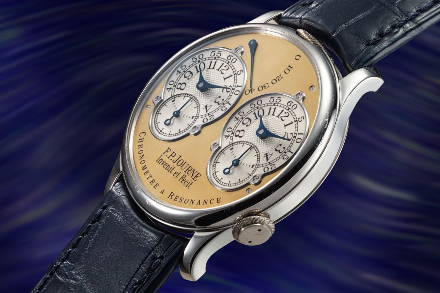 Orologio da polso di lusso con quadrante in oro e argento con quattro quadranti sovrapposti, lancette blu e cinturino in pelle nera, con la dicitura "F.P. Journe Chronomètre à Résonance". Lo sfondo è un motivo vorticoso di blu e viola.