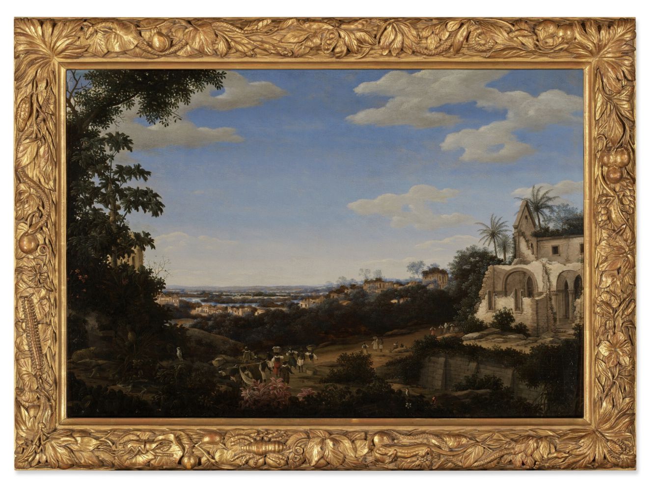 Un dipinto incorniciato raffigura un paesaggio panoramico con dolci colline, edifici lontani e un cielo blu con nuvole. Le persone camminano lungo un sentiero vicino a rovine antiche e a una vegetazione lussureggiante. La cornice ornata presenta un disegno a foglia d'oro.