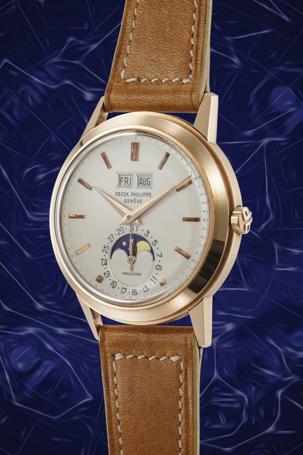 Orologio da polso Patek Philippe in oro con cinturino in pelle marrone, con indicazione di giorno, data, mese e fasi lunari su un quadrante bianco, su uno sfondo blu a motivi astratti.