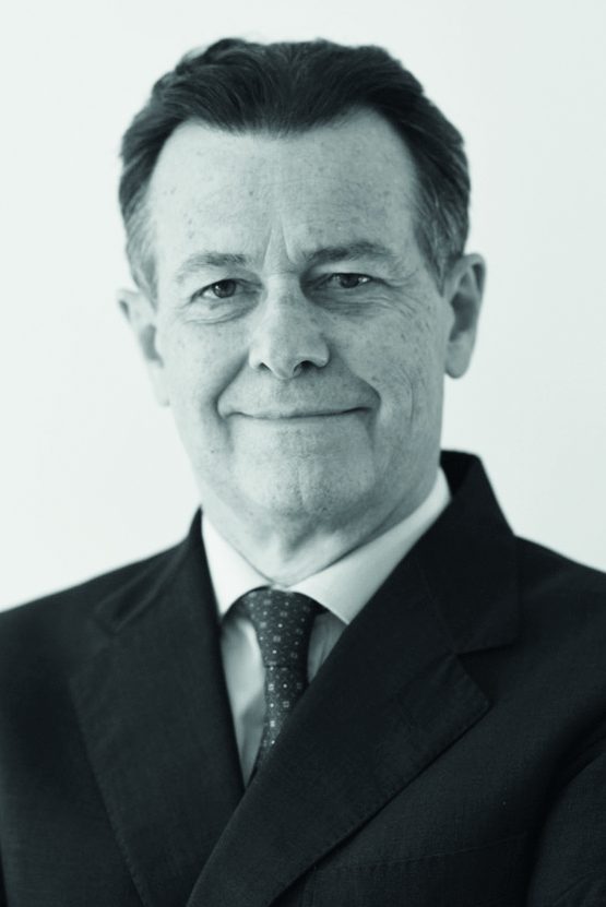 A middle-aged man with short dark hair, wearing a suit, dress shirt, and tie, is smiling slightly and looking at the camera against a plain light background.