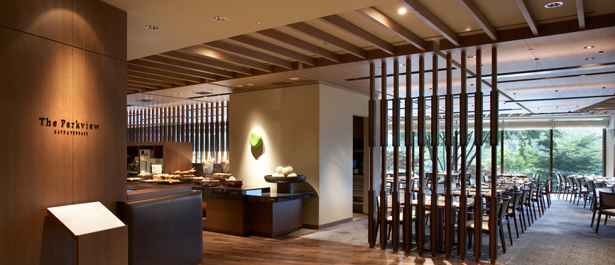 A modern, upscale restaurant interior with wooden accents, neatly arranged dining tables, soft lighting, and large windows overlooking greenery. A sign reads “The Parkview Café & Restaurant.”.