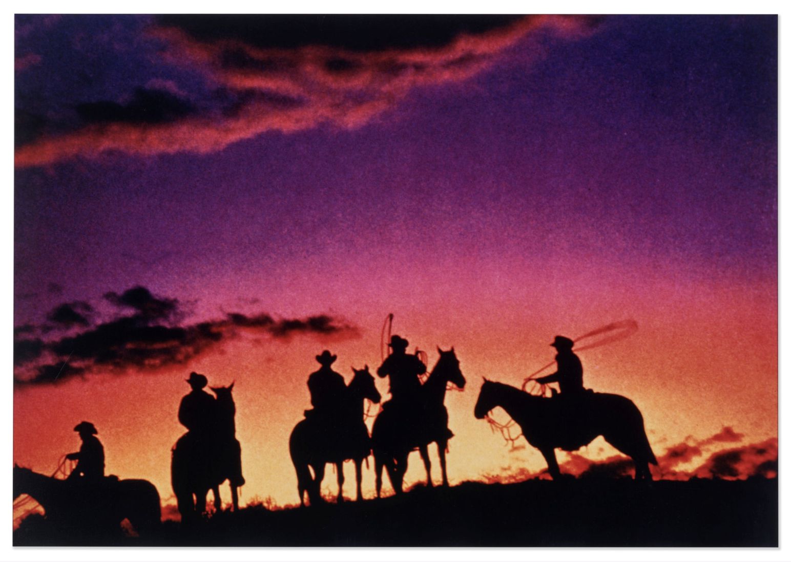 I cowboy a cavallo si stagliano su un drammatico cielo al tramonto, le cui vivaci tonalità arancioni, rosa e viola ricordano le splendide scene presenti nelle foto più costose 2025.