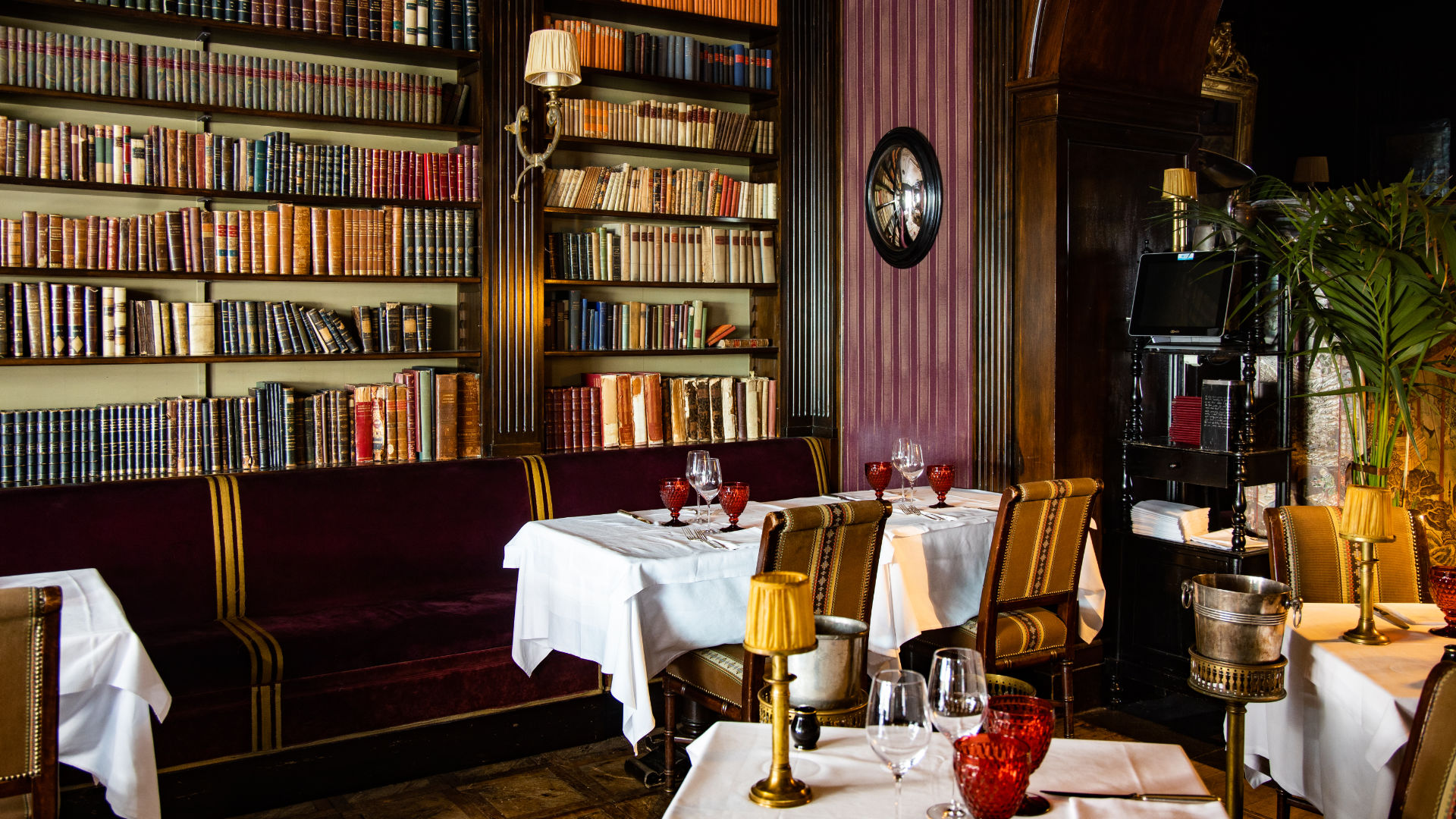 Elegante interno di un ristorante di Lugano con tavoli apparecchiati per la cena, con tovaglie bianche, bicchieri rossi, accenti dorati e librerie piene di libri alle pareti, che creano un ambiente accogliente e sofisticato.