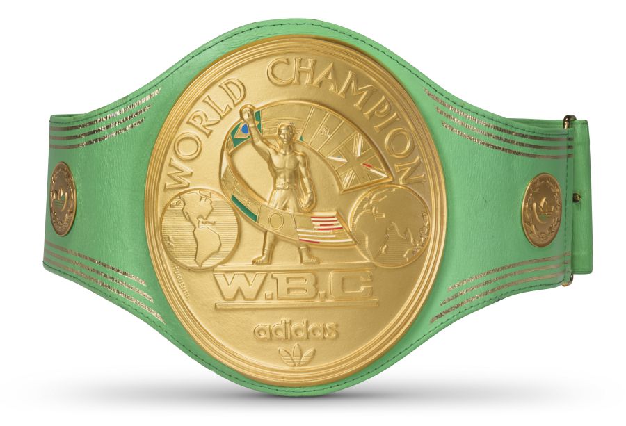 Una cintura da pugile campione del mondo WBC in oro e verde con l'illustrazione di un pugile, motivi di un globo, varie bandiere e il logo adidas sulla piastra centrale in oro: un pezzo di grande impatto per qualsiasi collezione rock.