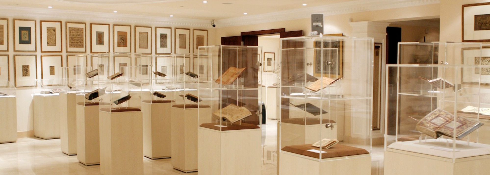 Una sala espositiva del museo espone collezioni di arte islamica, con libri e manoscritti antichi in teche di vetro, con documenti incorniciati sulle pareti color crema e un'illuminazione soffusa che illumina lo spazio.