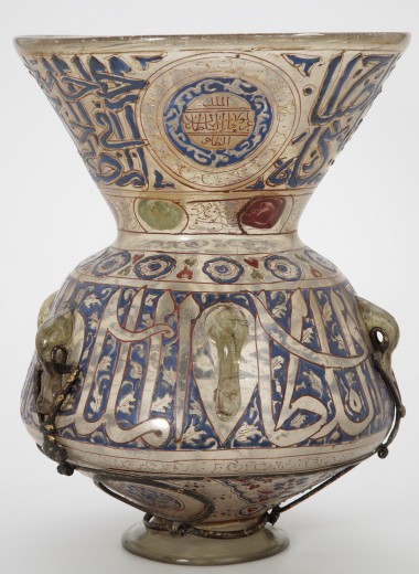 Grande lampada islamica in vetro di arte islamica collezioni con piano svasato, ornato da calligrafia araba blu e oro, medaglioni in smalto colorato, dettagli metallici e manici ad anello con decorazioni di teste di animali stilizzate.