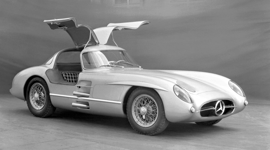 Una classica auto sportiva Mercedes-Benz argentata con le caratteristiche portiere ad ali di gabbiano aperte verso l'alto, fotografata in bianco e nero su uno sfondo a tinta unita, un'icona del design elegante nota per i suoi cerchi a raggi metallici e messa all'asta per un impressionante record di aste.