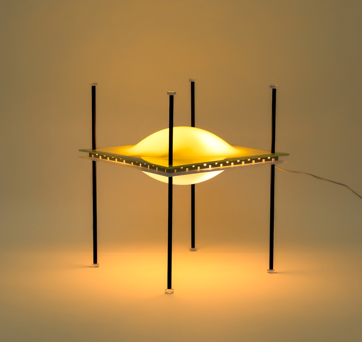 Una lampada moderna ispirata all'arte kruso presenta una luce incandescente a forma di cupola al centro, racchiusa da una cornice quadrata e sostenuta da quattro aste nere verticali, che emette una calda luce gialla in un ambiente minimalista.