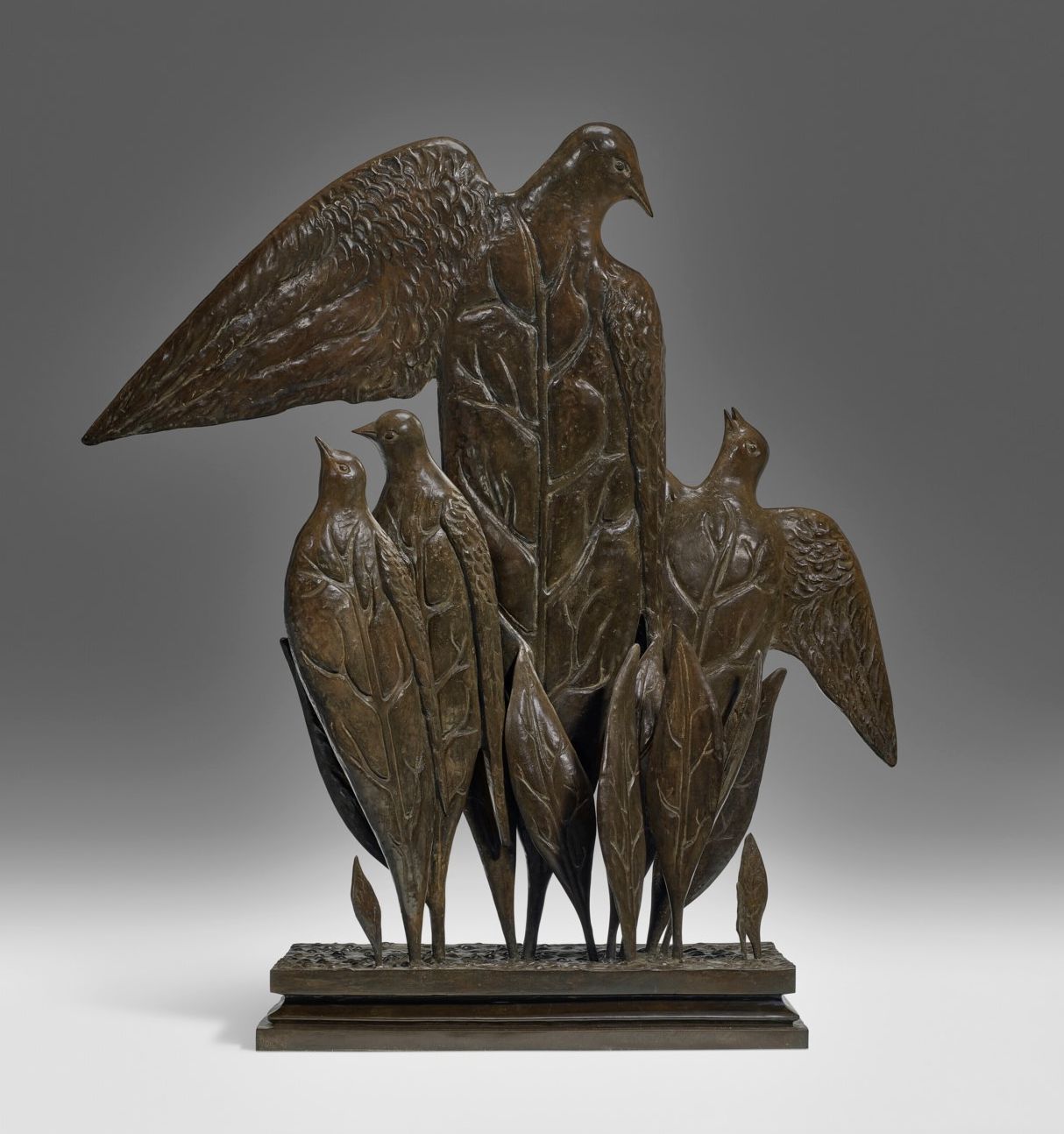 Una scultura in bronzo raffigura quattro uccelli stilizzati con corpi allungati e ali simili a foglie, ispirati a Magritte uccelli foglie, che si trovano insieme su una base rettangolare. Le ali di un uccello sono sollevate con grazia sopra il gruppo.