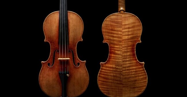 Due violini della collezione beni 2025 sono raffigurati su uno sfondo nero: uno mostra la parte anteriore con le corde e la tastiera, mentre l'altro rivela il retro, mettendo in evidenza le squisite venature del legno e la lavorazione artigianale.