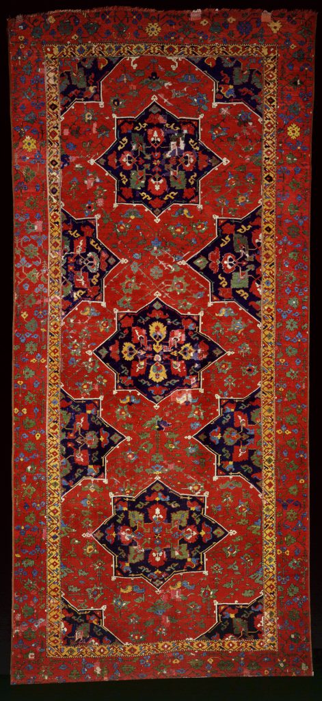 Un tappeto persiano riccamente decorato, con sfondo rosso e medaglioni geometrici, motivi floreali e intricati disegni di bordo nei toni del blu, dell'oro e del verde: un pezzo squisito per le collezioni di arte islamica.