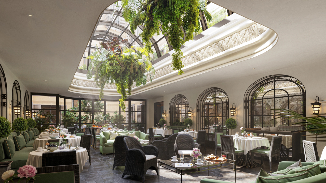Un ristorante interno a Lugano, luminoso ed elegante, con soffitto in vetro, rigogliose piante pendenti, sedie verdi con cuscini, tavoli rotondi per mangiare e luce naturale che entra dall'alto.