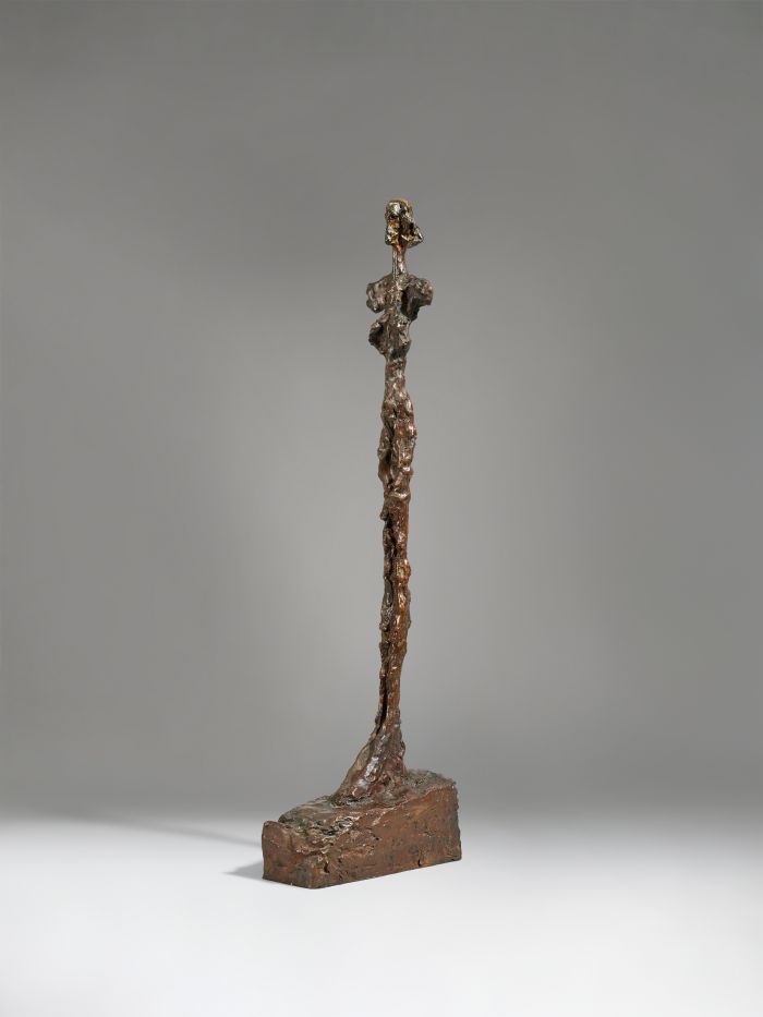 Una scultura in bronzo alta e slanciata di una figura femminile in piedi con arti allungati e dettagli minimali, che ricorda le opere viste nelle mostre di Lucio Fontana Milano, posizionata su una base rettangolare su uno sfondo grigio neutro.