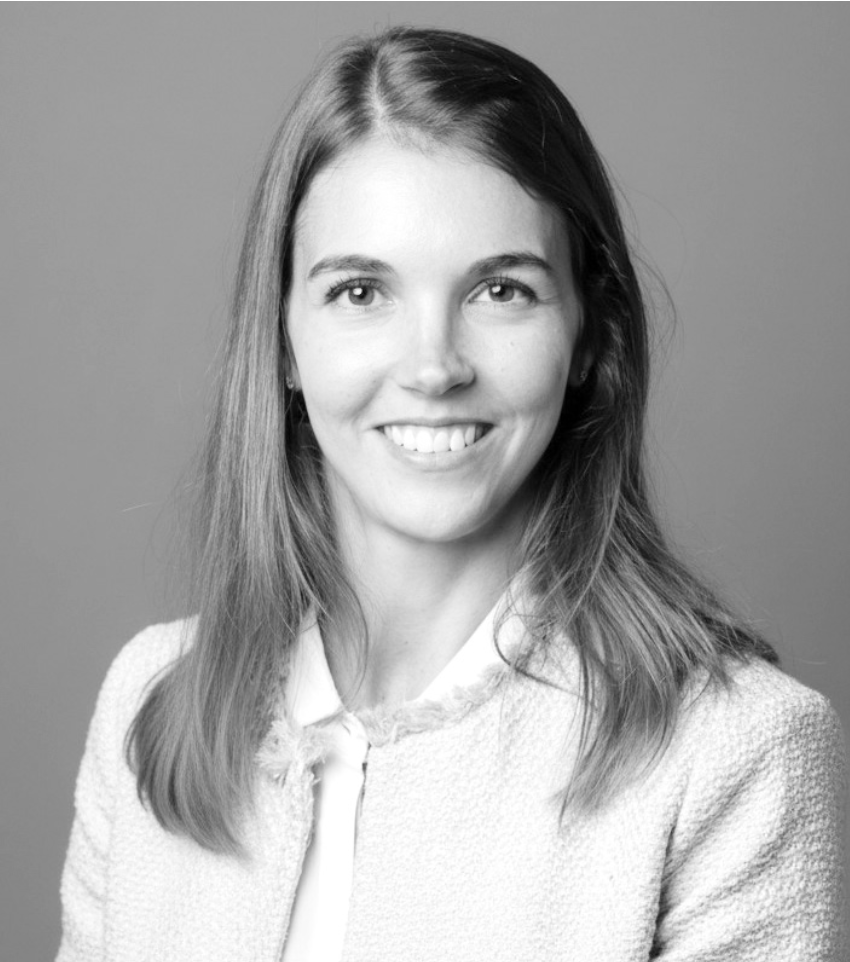 Ritratto in bianco e nero di una giovane donna dai lunghi capelli lisci, sorridente con un blazer strutturato su una camicia con colletto, in posa su uno sfondo semplice, che cattura perfettamente lo stile disinvolto di un weekend milanese.